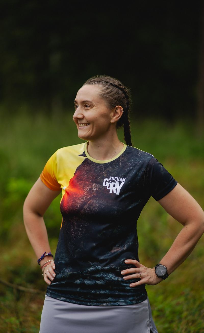 Lächelnde Frau in einem dunklen Laufshirt mit Bergmotiv