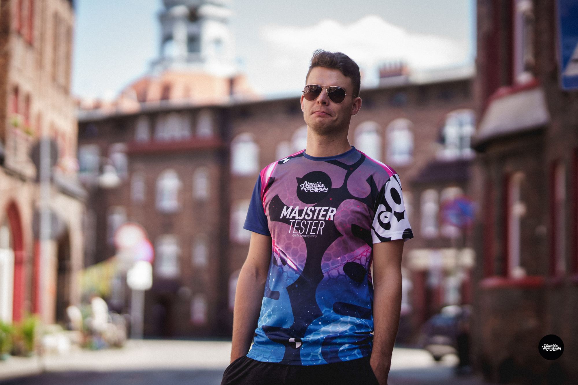 Mann in einem bunten sublimierten Laufshirt in einer Straße mit Backsteinhäusern